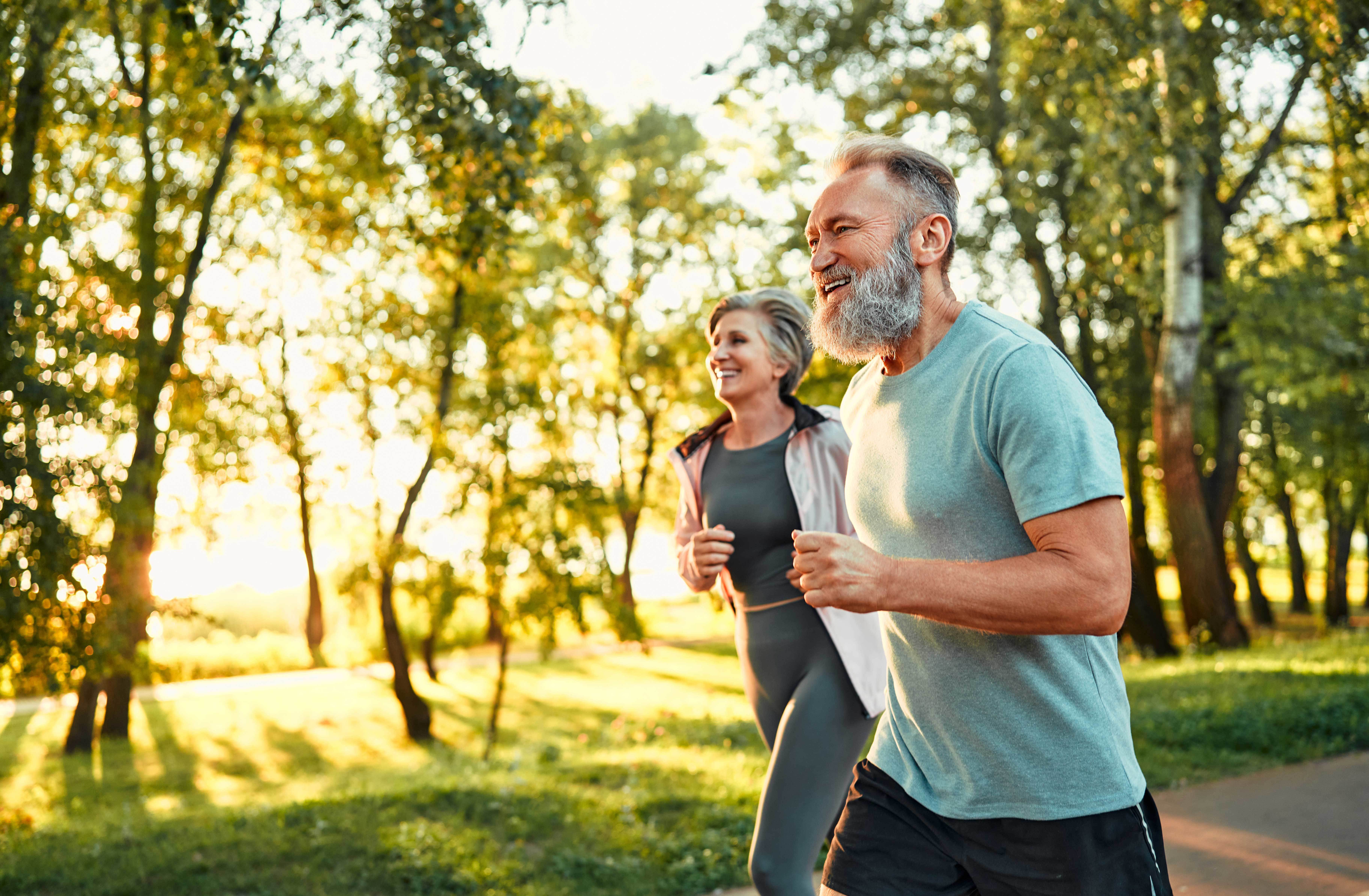 healthy male and female running through a park in the sun
