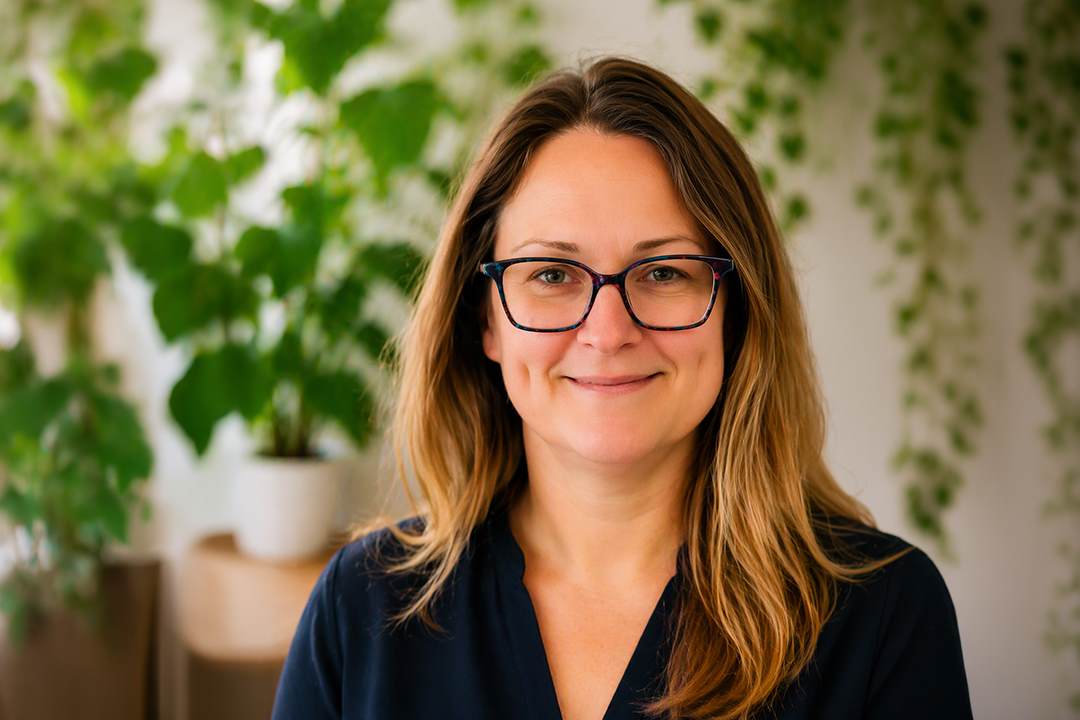 headshot of lady wearing glasses in front of a foliage wall