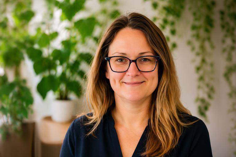 headshot of lady wearing glasses in front of a foliage wall