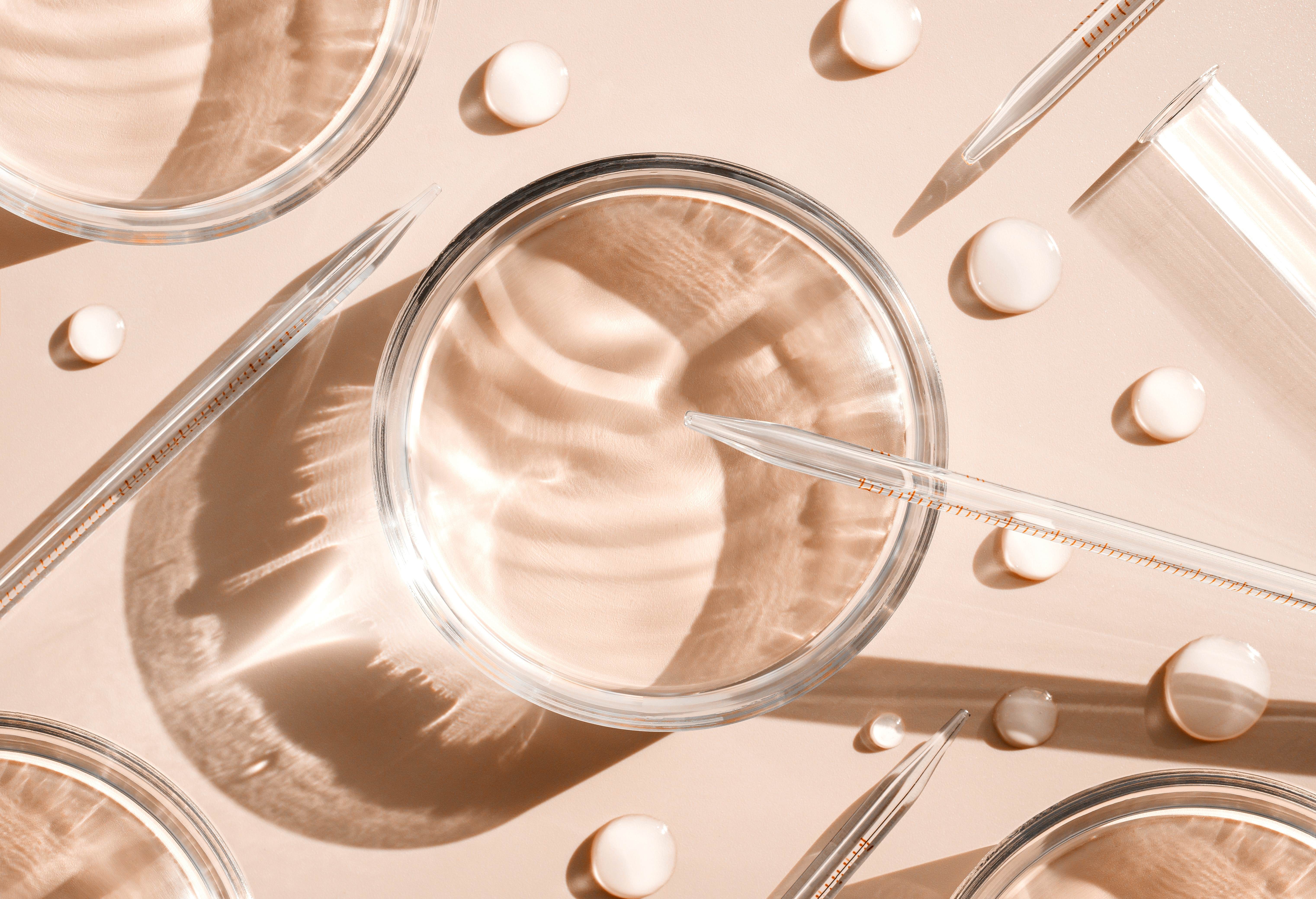 Overhead view of laboratory glassware and pipettes arranged on a soft neutral background, representing scientific innovation and beauty research.