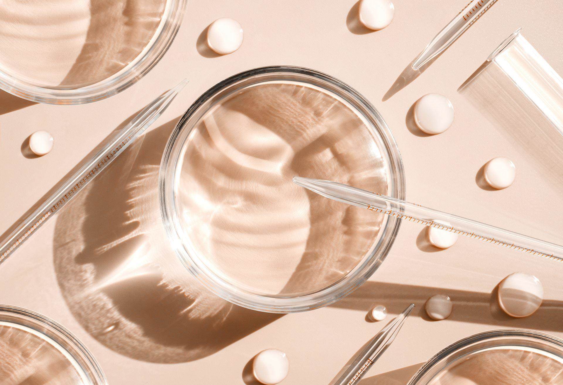 Overhead view of laboratory glassware and pipettes arranged on a soft neutral background, representing scientific innovation and beauty research.