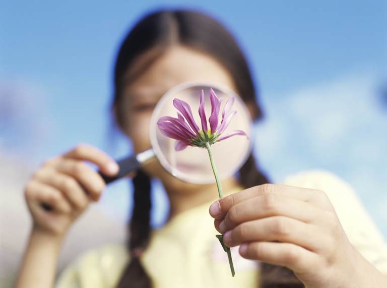 Woman looking at a flower under a magnifying glass.