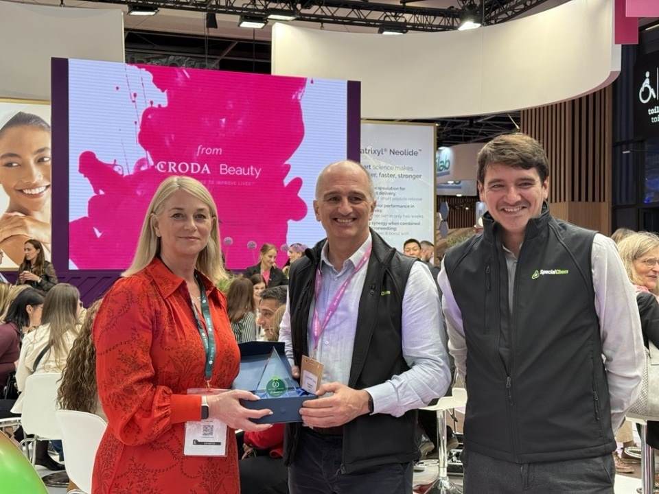 a lady and two men stood in front of exhibition receiving an award